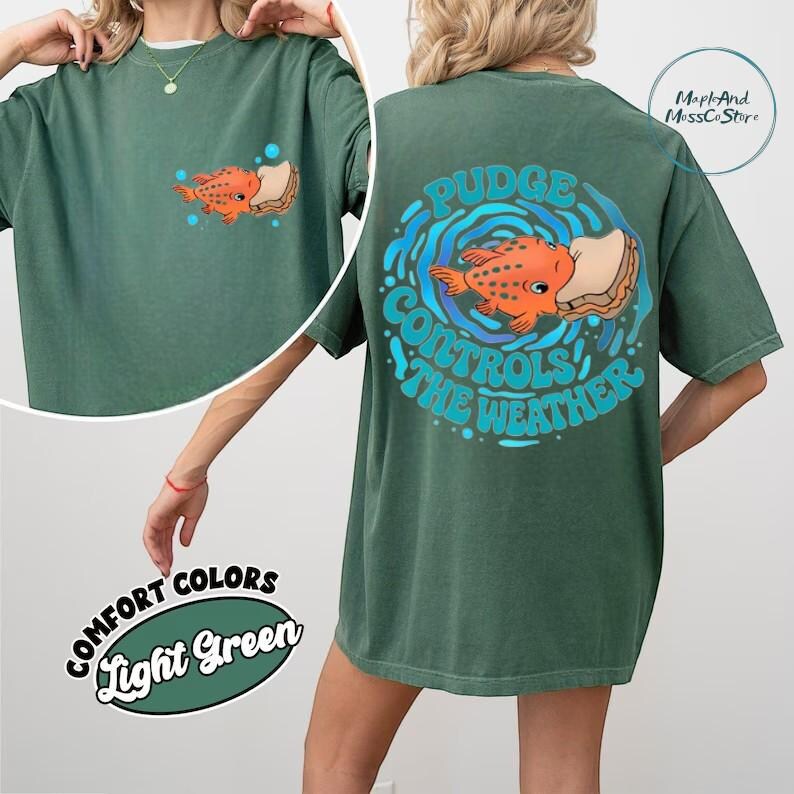 A green t-shirt with a graphic design featuring an orange fish and the text "Pudge Control The Weather" printed on the back.