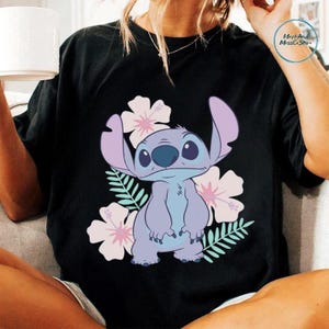 A person wearing a black t-shirt with a graphic of a cartoon character surrounded by flowers and leaves.