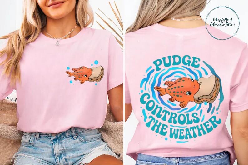 A woman wearing a pink t-shirt with a cartoon fish and the text "Pudge Controls the Weather" printed on it.