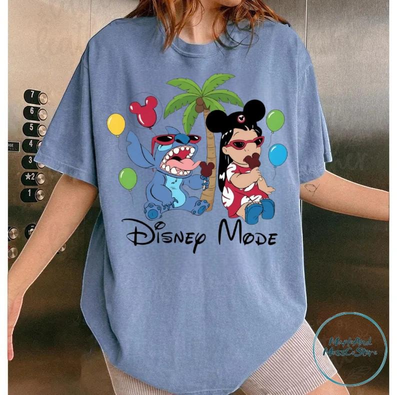 A person wearing a blue t-shirt with a graphic design featuring characters from the Disney movie "Stitch" and the text "Disney Mode".