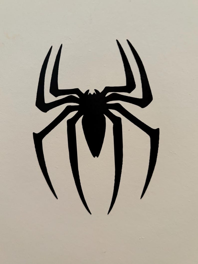May include: A black spider emblem with eight legs, a segmented body, and a pointed head. The spider is centered on a white background. The spider's legs are long and curved, with pointed tips.