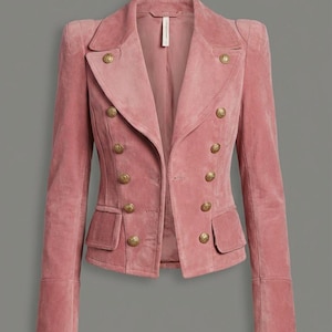May include: A dusky pink blazer with a double-breasted design. The jacket features gold-coloured buttons, two front pockets, and a tailored fit. The sleeves have a cuff detail. The blazer is made of a soft, velvety material.