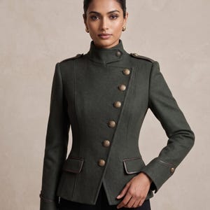 K&ouml;nnte beinhalten: Dunkelgr&uuml;ne Jacke im Milit&auml;rstil mit hohem Kragen und asymmetrischem Knopfverschluss. Die Jacke hat goldfarbene Kn&ouml;pfe, braune Lederbes&auml;tze und Schulterklappen. Die taillierte Passform und das strukturierte Design sorgen f&uuml;r einen raffinierten Look.