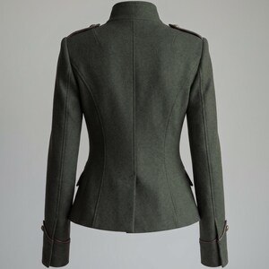 K&ouml;nnte beinhalten: Dunkelgr&uuml;ne Jacke im Milit&auml;rstil mit hohem Kragen und langen &Auml;rmeln. Die Jacke hat braune Akzente an Schultern, Manschetten und Taschen. Die taillierte Passform umfasst eine schmale Taille und dekorative Kn&ouml;pfe.