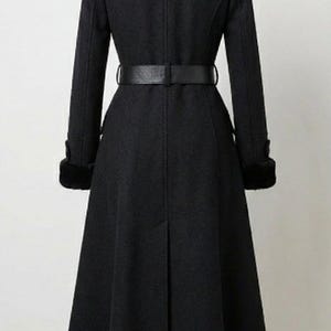 May include: A long, black coat with a wide collar and a matching belt cinching the waist. The coat features long sleeves with fur cuffs and a flared skirt, creating an elegant silhouette. The coat is a classic design.