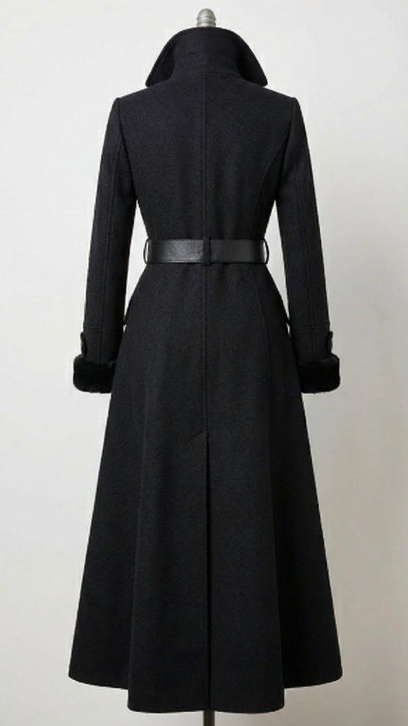 May include: A long, black coat with a wide collar and a matching belt cinching the waist. The coat features long sleeves with fur cuffs and a flared skirt, creating an elegant silhouette. The coat is a classic design.