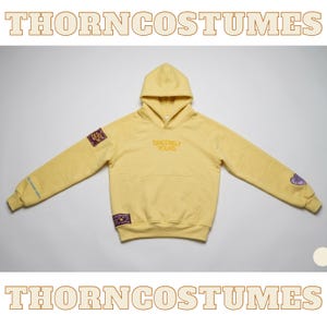 Puede incluir: Una sudadera con capucha amarilla con capucha y bolsillo delantero. La sudadera tiene la inscripción bordada "Sincerely Yours" en el pecho y parches en las mangas. Las mangas también tienen texto y parches en forma de corazón. Se muestra la marca "THORNCOSTUMES".