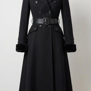 May include: A long, black wool coat with a double-breasted design, featuring a wide collar, a belted waist, and faux fur cuffs. The coat has a classic, tailored silhouette, with a flared skirt and button details.