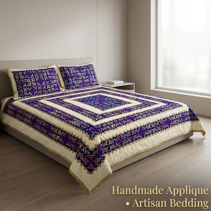 May include: Cream-colored bedding set with a geometric pattern in shades of blue, purple, and gold. The set includes a comforter and two pillowcases. The text "Handmade Applique - Artisan Bedding" is visible.