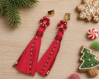 May include: A pair of long dangle earrings featuring vibrant red thread tassels, accented with small red faceted beads and gold-toned metal hardware. The design includes a circular bead cluster at the top, connecting to a long, flowing red tassel.
