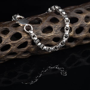 May include: A silver chain bracelet with a clasp closure. The bracelet is lying on a brown, textured surface.