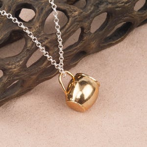 May include: A gold-tone necklace with a small, detailed, gold-tone pitcher pendant.