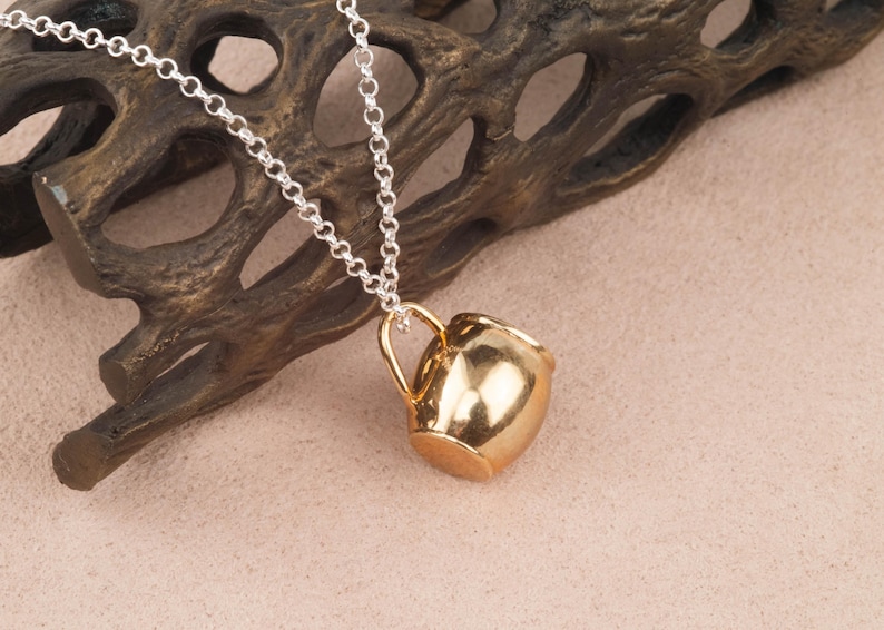 May include: A gold-tone necklace with a small, detailed, gold-tone pitcher pendant.