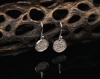 May include: A pair of silver dangle earrings with a circular Celtic knot design. The earrings are hanging from a wooden surface.