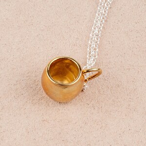 May include: A gold-colored mug pendant necklace with a silver chain. The mug is a small, detailed replica of a traditional mug.