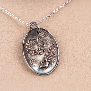 May include: A silver necklace with an oval pendant featuring a Celtic knot design and a stylized fish. The pendant is detailed and intricate.