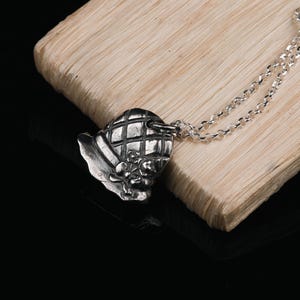 May include: A silver necklace with a detailed pendant shaped like a hat with a floral design.