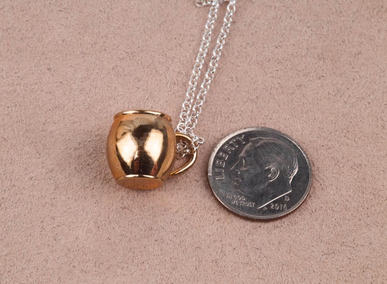 May include: A gold-toned mug pendant necklace on a silver chain. The pendant is about the size of a dime.