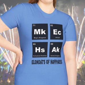 May include: A light blue t-shirt with a graphic design featuring the text "ELEMENTS OF HAPPINESS". The design includes four black squares with the abbreviations "MK", "Ec", "Hs", and "Ak", representing Magic Kingdom, EPCOT, Hollywood Studios, and Animal Kingdom.