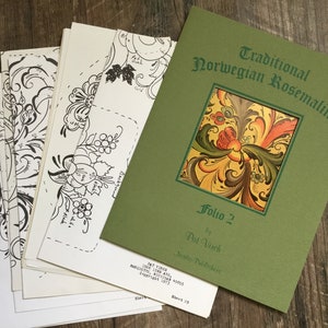 以下が含まれることがあります： 「Traditional Norwegian Rosemaling, Folio 2 by Pat Vleck, Nordic Publishers」というタイトルの緑色の本で、表紙にはカラフルな花柄のデザインが施されています。この本には、白黒の線画の束が付属しています。