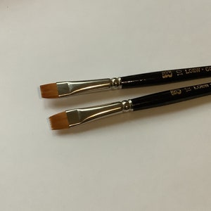 May include: Two flat paint brushes with black wooden handles and silver ferrules. The brushes are labeled "10 Loew-Cor" and "10 Loew-Cor".