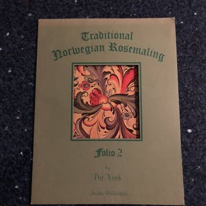 以下が含まれることがあります： 「Traditional Norwegian Rosemaling Folio 2」と題された緑色の本の表紙。Pat VirchとNordic Publishersによる。表紙には、赤、オレンジ、黄色、緑、黒のカラフルな花柄が描かれている。