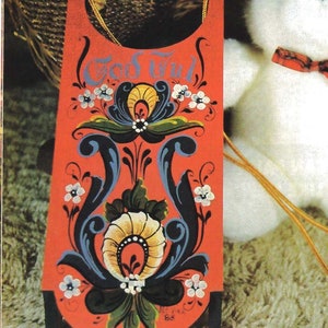 May include: A red wooden sled with a painted design of flowers and swirls. The sled is decorated with the words "God Jul" in blue and white lettering. The sled is sitting on a white fluffy surface.