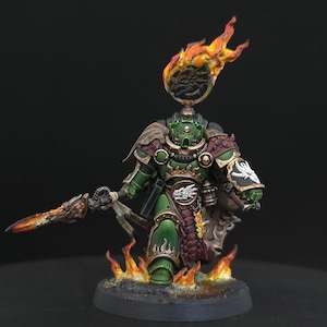 May include: A green armored warrior miniature featuring gold trim, a dragon emblem on the chest, and a flaming spear. The figure wears a dark cloak, stands amidst sculpted flames, and has a circular icon with a dragon head topped by fire.