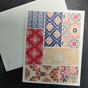 May include: A handmade greeting card with a patchwork design. The card features various patterned paper squares in red, blue, yellow, and white. An envelope is included. The card is suitable for various occasions.