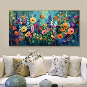 May include: A vibrant floral painting featuring a variety of colorful flowers in shades of yellow, orange, pink, purple, and blue. The artwork is framed in a gold-colored frame and hangs above a white sofa with decorative pillows.
