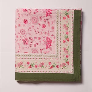 Può includere: Un tessuto quadrato con un centro rosa chiaro e un motivo floreale rosa scuro. È incorniciato da un bordo beige con un disegno ripetitivo di viticci floreali rosa e rifinito con un bordo solido verde oliva scuro sui lati destro e inferiore.