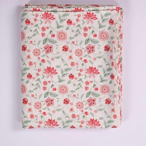 May include: A folded rectangular textile featuring a cream-colored background with a repeating floral pattern. The design consists of stylized red and pink flowers, buds, and green leafy vines distributed evenly across the entire fabric surface.