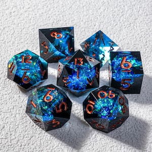 Könnte beinhalten: Set aus sieben polyedrischen Würfeln mit schwarzer Basis und blau-grünem Innendesign. Die Zahlen sind kupferfarben. Die Würfel sind für Rollenspiele.