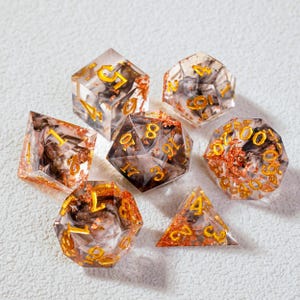 Può includere: Set di sette dadi poliedrici per giochi da tavolo. I dadi sono trasparenti con un interno a vortice marrone e oro e numerazione dorata. Include un d4, d6, d8, d10, d12, d20 e un dado percentuale.