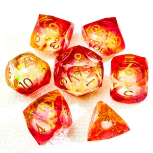 Peut inclure: Ensemble de sept dés polyédriques rouges et dorés. Chaque dé présente des chiffres dorés et un intérieur chatoyant et irisé. Ces dés sont conçus pour les jeux de rôle sur table.