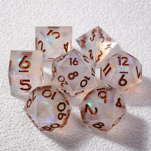 May include: A set of seven polyhedral dice with a pearlescent, iridescent effect. The dice have copper-colored numbers and are in various geometric shapes, including a d4, d6, d8, d10, d12, d20, and a percentile die.