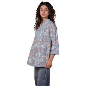 May include: A light blue tunic featuring a repeating floral pattern in shades of pink, white, and green. The garment has three-quarter length sleeves, a mandarin collar, and a button-down front placket. It is paired with dark blue denim jeans.