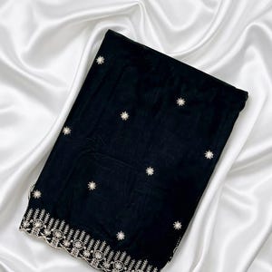 May include: A folded black fabric piece featuring scattered white embroidered star motifs across the surface and a wide, scalloped bottom border decorated with intricate white floral and leaf embroidery patterns along the finished edge.