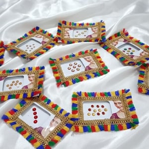 May include: Nine rectangular decorative frames with colorful fringed edges and gold trim are arranged on a white satin surface. Each frame features a small image of a woman and a collection of small, colorful embellishments.