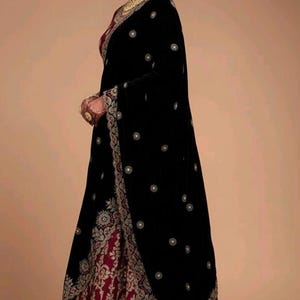 Puede incluir: Un vestido formal de terciopelo negro con intrincados bordados y adornos dorados. El vestido presenta un forro rojo oscuro y un chal a juego. El diseño es tradicional y elegante, adecuado para ocasiones especiales.