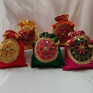 Puede incluir: Una colección de coloridas bolsas decorativas. Cada bolsa es de un color diferente, incluyendo rojo, amarillo, verde y rosa. Cuentan con intrincados bordados y adornos dorados, con cierre de cordón.