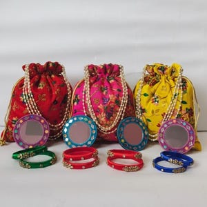Puede incluir: Tres bolsas con cordón en patrones florales rojos, rosas y amarillos, cada una con un collar de perlas. Acompañando las bolsas hay espejos redondos con bordes decorativos y juegos de pulseras en verde, rojo y azul.