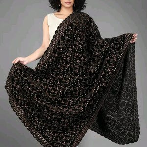 May include: A black velvet shawl with intricate floral embroidery and a scalloped edge. The shawl is draped over the shoulders, showcasing its rich texture and design. The embroidery features delicate gold-colored thread.