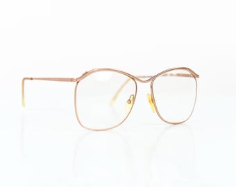 Könnte beinhalten: Eine Brille in Roségold mit einem abgerundeten quadratischen Gestell und klaren Gläsern.