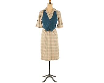 May include: A plaid dress with a teal vest on a mannequin. The dress has a short sleeve and a knee-length skirt.