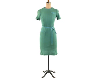May include: A green short-sleeved dress with a blue belt and a pocket on the left side.