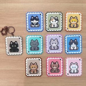 May include: A collection of colorful cat-themed Perler bead creations. The designs include various cat portraits in different colors, each framed within a square border. A star-shaped keychain is also included.