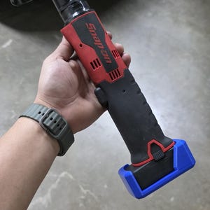 May include: A black, red, and blue Snap-on cordless ratchet wrench. The tool has a black handle with a red top and a blue base. The Snap-on logo is visible on the side.