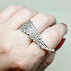 May include: A silver ring shaped like a wing with detailed feather patterns.
