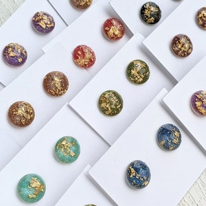 May include: Assortment of round resin earrings with gold leaf accents. The earrings are displayed on white cards.